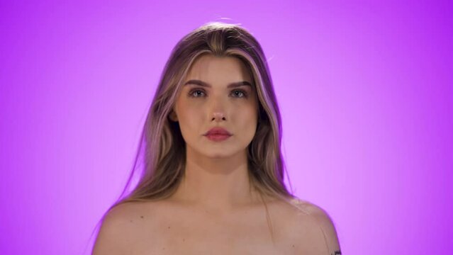 Medium shot of a young pretty woman ruffling through her hair before getting ready to go out in front of purple background in slow motion