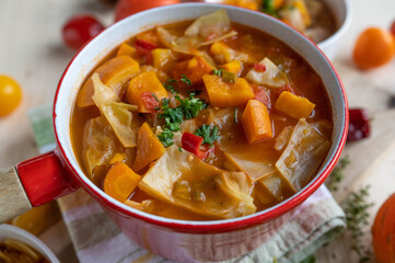Cabbage soup with pumpkin, carrots and tomatoes in a red pot
