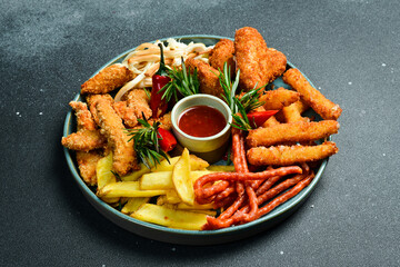 Fast food. Plate with snacks: nuggets, sausages, French fries, cheese sticks. On a black stone background. Free space for text.