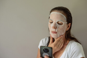 woman with a fabric cosmetic mask on her face, does skin care. Close-up portrait on a gray background. beauty industry, self-care.