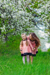 mother and daughter walk through a blooming apple orchard