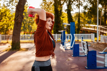 Healthy lifestyle. Mid adult happy Caucasian ginger hair woman is doing sports using dumbbells....