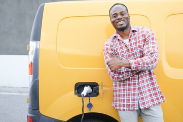 A african american man stands next to yellow electric delivery van at electric vehicle charging stations