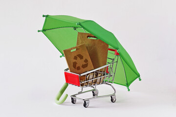 Shopping cart with paper shopping bag with recycling symbol under green umbrella - Concept of ecology and green shopping - 653615499
