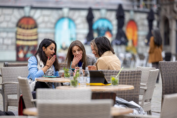 A vibrant group of young and diverse businesswomen gathers at an inviting outdoor setting in a picturesque European city. In this delightful scene, they savor cocktails, engage in lively conversation