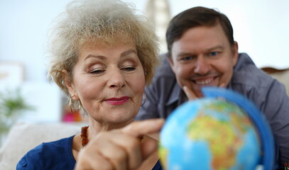 Close-up of senior woman and middle-aged man explore globe. Mother and son choose country for...
