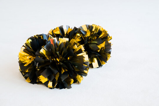 Gold and black cheerleading pom-poms on white practice mat