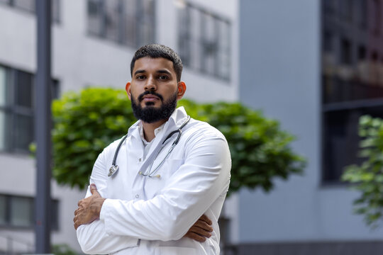 Portrait of a confident Muslim male doctor standing outside a hospital and looking seriously into the camera with his hands folded across his chest