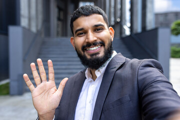 Close-up photo. Young Muslim businessman talking and greeting to the camera, standing outside on the street near the office center