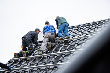 Team of technicians standing on the solar panel mounting rack on the roof of a house
