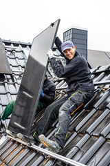 Smiling technician during installation of a solar panel on the roof of a house