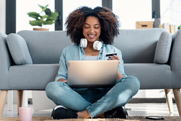 Relaxing woman paying something online with her credit card with laptop while sitting on the floor in living room at home