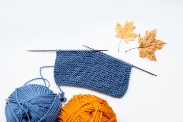 A piece of cloth knitted with blue threads and two balls of blue and yellow threads on a white background 