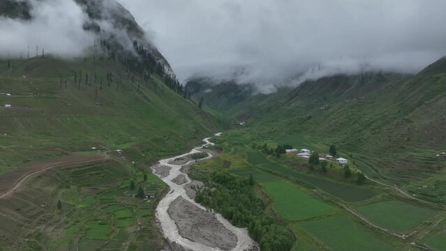 Accending and then follow drone shot over the calming lake and lush green valley in Northern area of Pakistan on a cloudy day