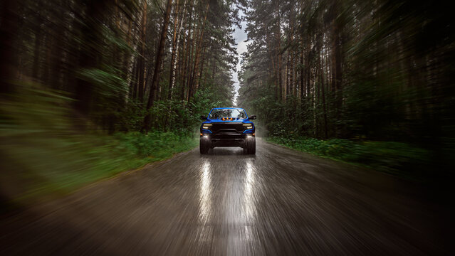 A blue new pickup truck is driving along a highway in the forest with a blurred background. Fast driving