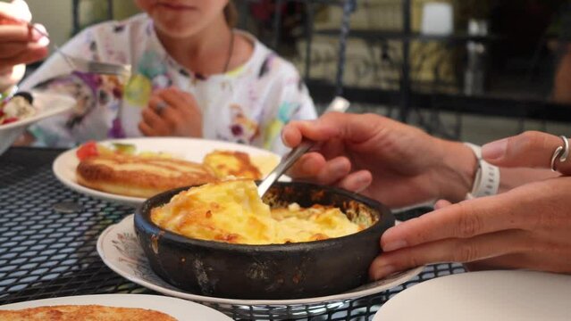 A close-up of a woman's hand takes from ketsi a Georgian traditional dish, Borano (cheese omelet) and placing it onto her plate