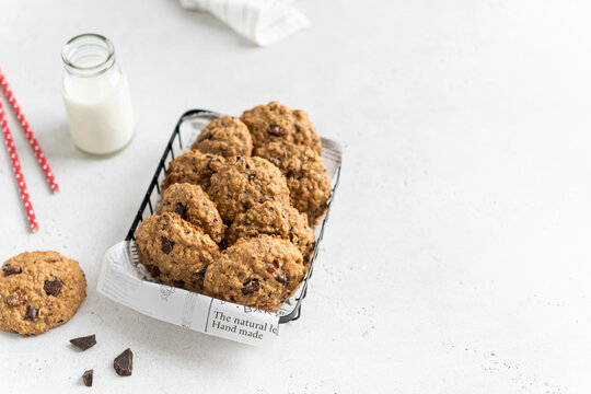 Healthy oat cookies in a basket and bottle of milk on white background. Homemade flour free oatmeal cookies with banana, oats, nuts, eggs and chocolate drops. Gluten free oatmeal biscuits. Copy space