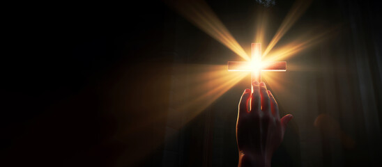 Hand reaching for the cross with light rays on a dark background. Copy space - obrazy, fototapety, plakaty