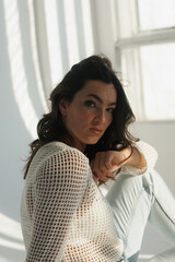 Beautiful brunette woman in white net top and blue jeans, sitting. Girl smile, happy. Portrait of...