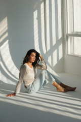 Beautiful brunette woman in white net top and blue jeans, sitting. Girl smile, happy. Portrait of...