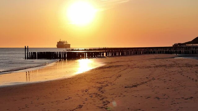 In the distance large ship sits moored on an idyllic coastline. Beautiful golden hour sky