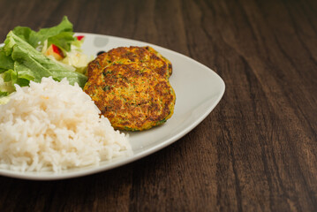 Oatmeal fritters with vegetables and white rice served on a plate on a wooden table. Healthy food.