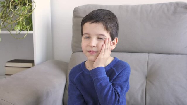 Stressed child complaining suffering toothache sitting on a couch at home