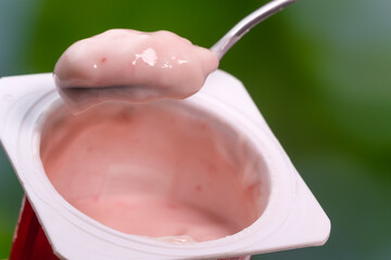 Close-up of a teaspoon with pink yogurt in a cup, macro photography