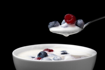 Spoon with greek yogurt and blueberries, raspberries over a white bowl on a black background, macro photography. Delicious healthy breakfast made from natural ingredients