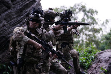 Fototapeta premium Military army soldiers tactical team, commando group moving cautiously in forest area, kneeling and looking around, covering comrades, controlling sectors. Commander showing halt or stop hand signal