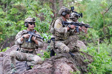 Fototapeta premium Military army soldiers tactical team, commando group moving cautiously in forest area, kneeling and looking around, covering comrades, controlling sectors. Commander showing halt or stop hand signal