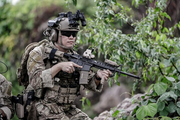 Fototapeta premium Military army soldiers tactical team, commando group moving cautiously in forest area, kneeling and looking around, covering comrades, controlling sectors. Commander showing halt or stop hand signal