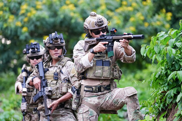 Fototapeta premium Military army soldiers tactical team, commando group moving cautiously in forest area, kneeling and looking around, covering comrades, controlling sectors. Commander showing halt or stop hand signal