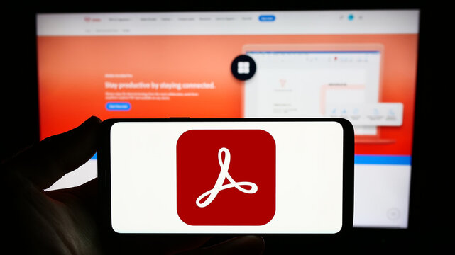 Stuttgart, Germany - 09-23-2023: Person holding smartphone with logo of PDF management software Adobe Acrobat on screen in front of website. Focus on phone display.