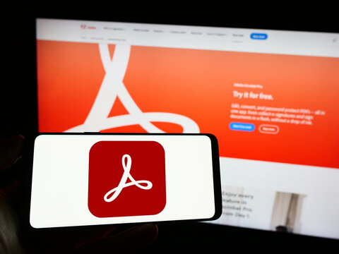 Stuttgart, Germany - 09-23-2023: Person holding mobile phone with logo of PDF management software Adobe Acrobat on screen in front of company web page. Focus on phone display.
