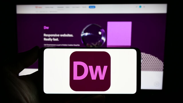 Stuttgart, Germany - 09-23-2023: Person holding smartphone with logo of web development software Adobe Dreamweaver on screen in front of website. Focus on phone display.