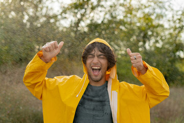Happy arab guy enjoying the weather in the rain in a yellow raincoat resting in the park