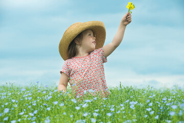 Adorable smiling child in a straw hat with a bouquet of yellow flowers in the middle of a beautiful field of flowers. - 653680604