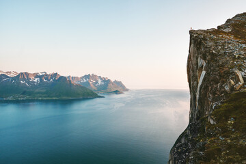 Norway landscape man standing on cliff rock edge above fjord Senja mountains travel hiking...