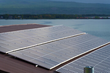 Close-up of solar panels on the roof of a house on the background of a lake, mountains