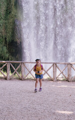 little girl in front of a waterfall with a hiker's backpack and binoculars looking at the camera and laughing