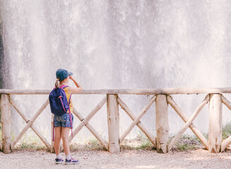 little girl in front of a waterfall wearing a cap with a hiker's backpack and binoculars. General plane, copy space.