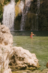little girl bathing in a natural pool with a waterfall in the background, she is in the middle of the mountain with a pink swimsuit. Playing and having fun.