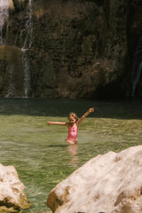 little girl bathing in a natural pool with a waterfall in the background, she is in the middle of the mountain with a pink swimsuit. Playing and having fun.
