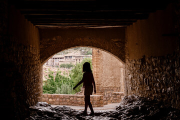 little girl walking against the light under a bridge, only her silhouette can be seen. Horizontal view in an old town of Spain