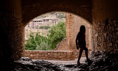 little girl walking against the light under a bridge, only her silhouette can be seen. Horizontal view in an old town of Spain