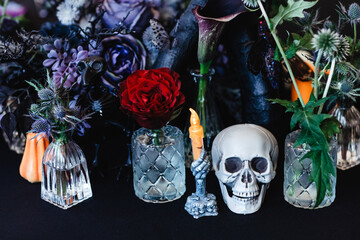 Halloween table arrangement with skull, candle, red and blue roses and thorny plants in a dark colour scheme.