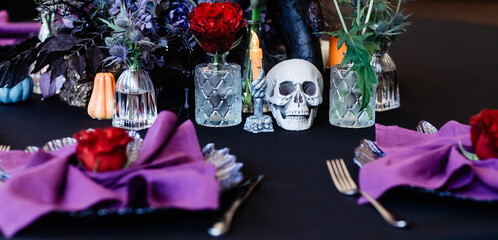 Festive Halloween table setting in black, purple and red colours with roses, skull and prickly plants.