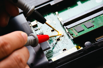 Electrician checks electronic circuit board by probe of digital multimeter. Technician checks and diagnoses problems with computer motherboards. Appliance repair concept - obrazy, fototapety, plakaty