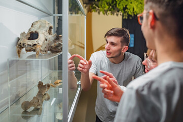 Curious young people observing animal skeletons and skulls displayed in a showcase during natural...